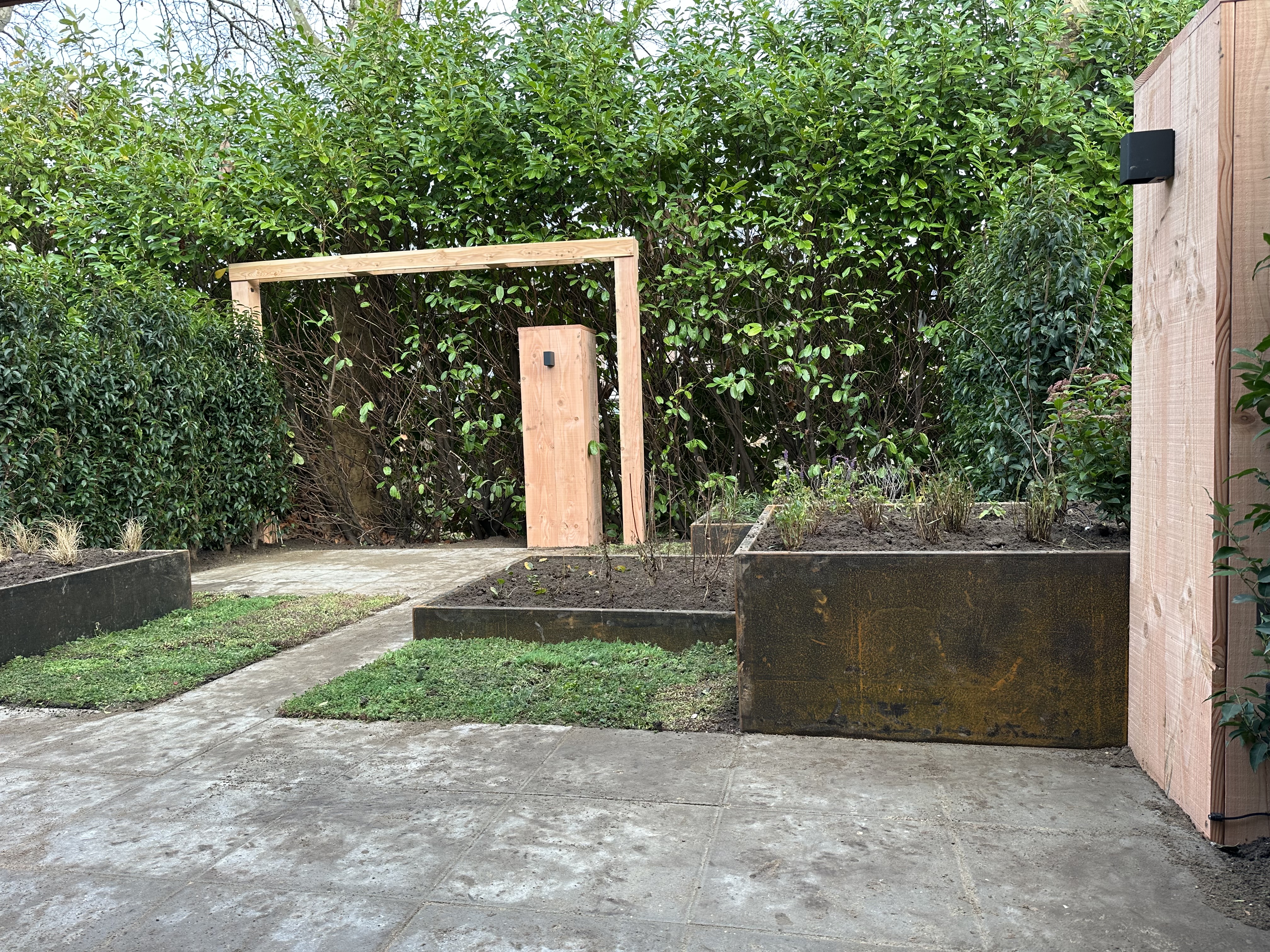 Tuin met cortenstalen bakken, houten pergola en betonnen tegelvloer