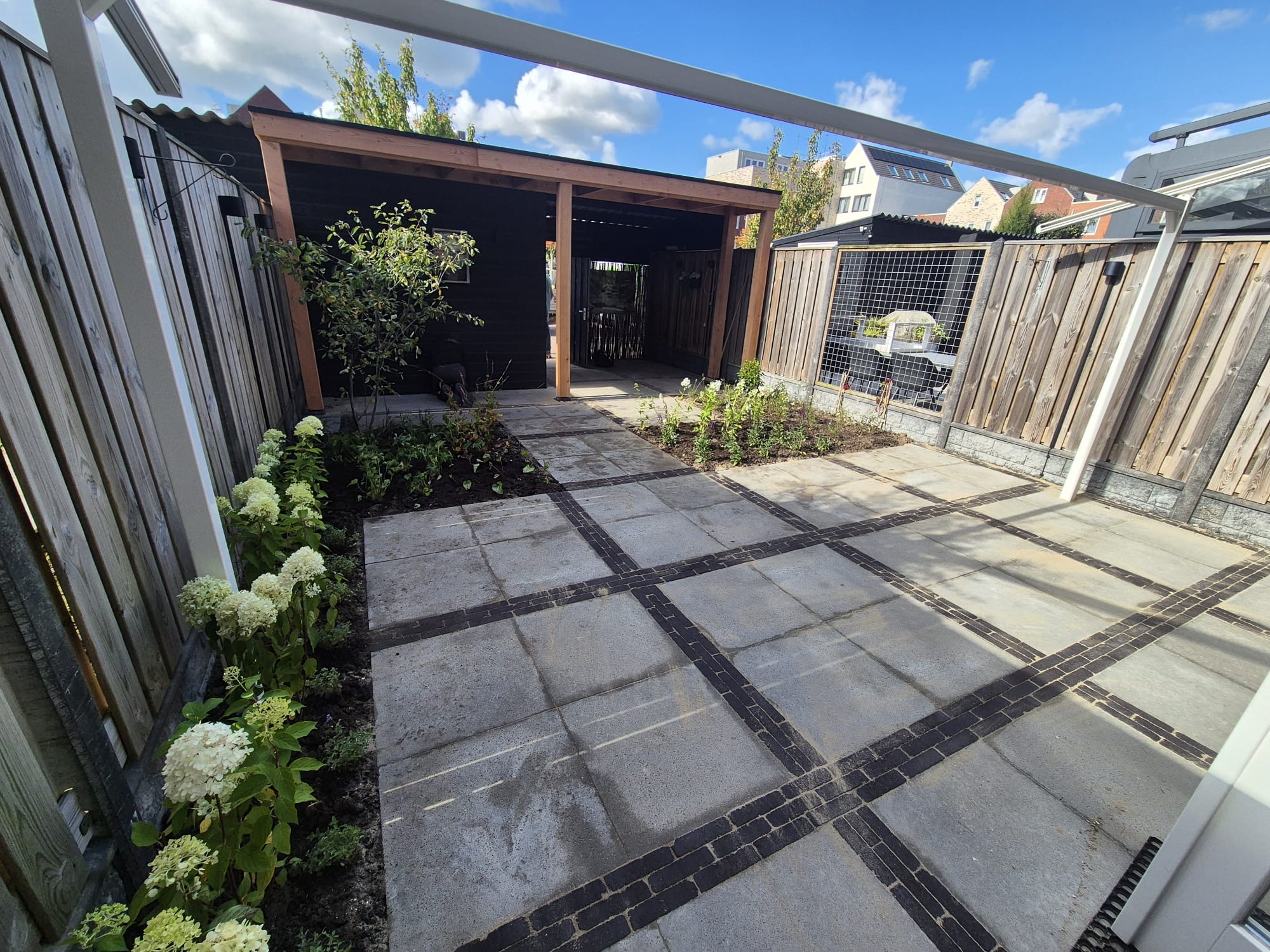 Ruime achtertuin met grote tegels, houten overkapping en hortensia-borders