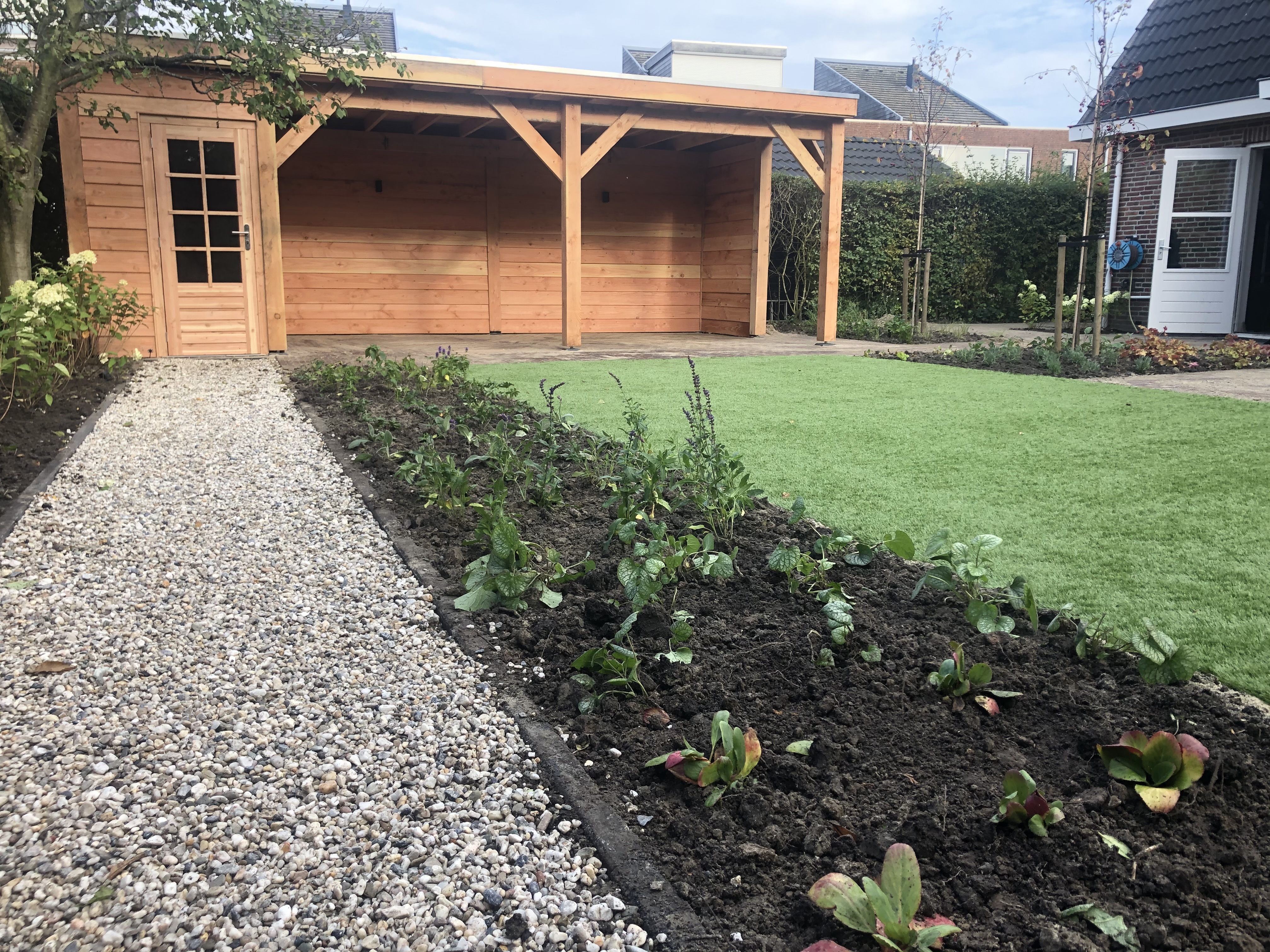 Landelijke tuin met houten schuur, overkapping en verse beplanting